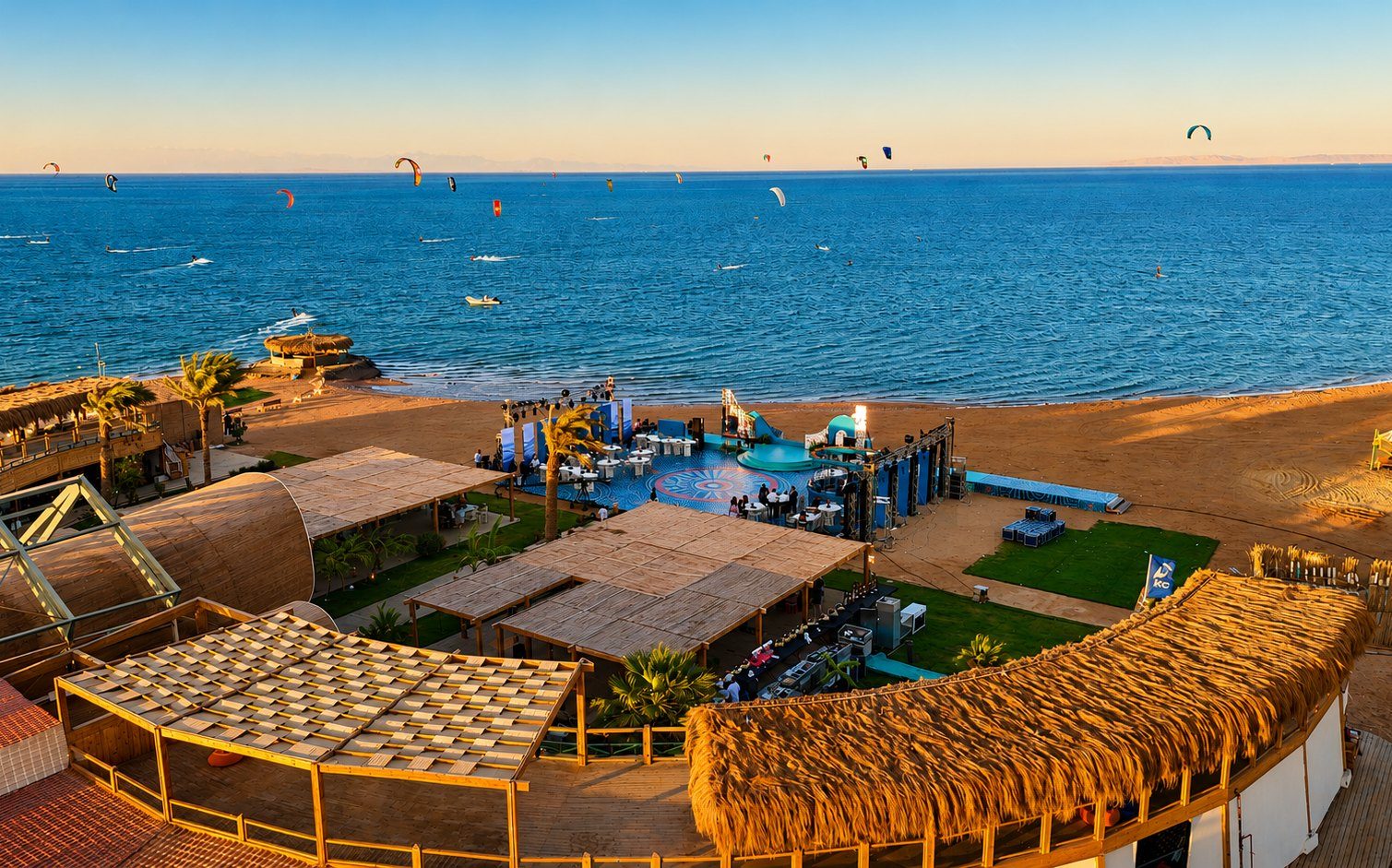 Aerial view of Riah's beachfront wedding venue in El Gouna at golden hour, with the event stage on the sand and kites over the Red Sea