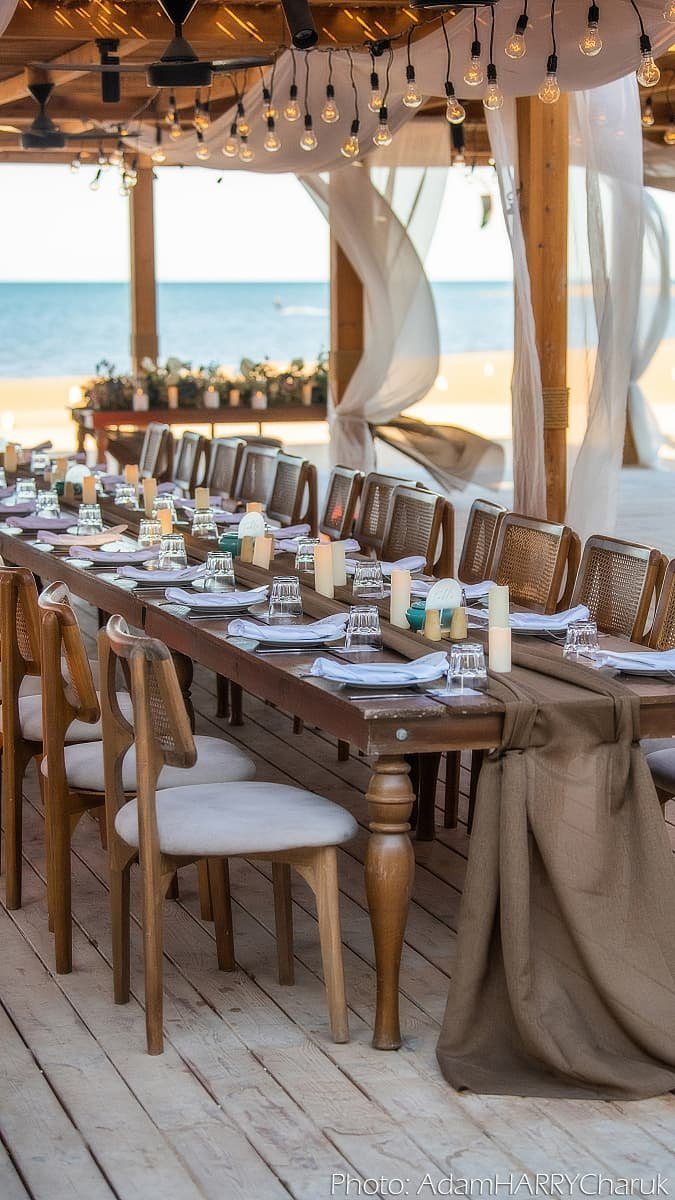 Long dinner table set under a draped pergola facing the sea